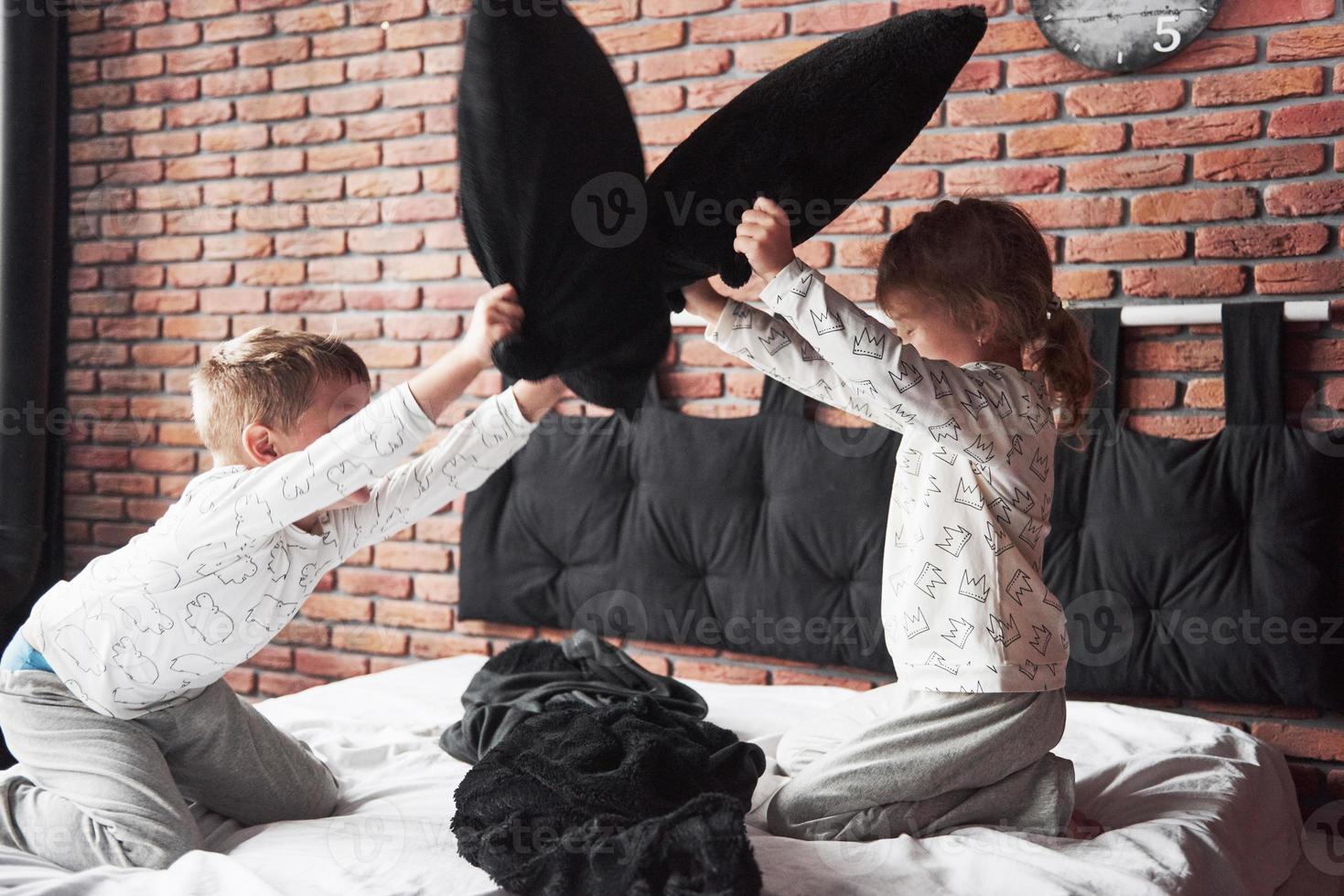 stoute kinderen kleine jongen en meisje voerden een kussengevecht op het bed in de slaapkamer. ze houden van dat soort spel foto