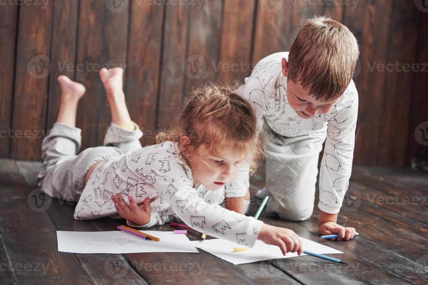 kinderen liggen in pyjama op de grond en tekenen met potloden. schattig kind schilderen met potloden foto