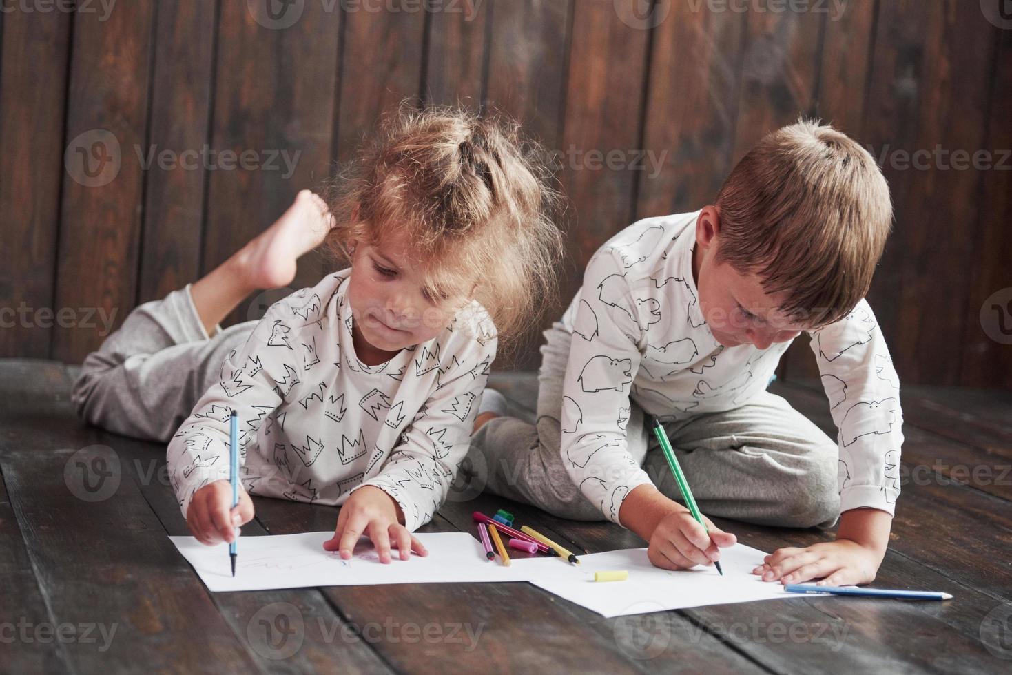 kinderen liggen in pyjama op de grond en tekenen met potloden. schattig kind schilderen met potloden foto