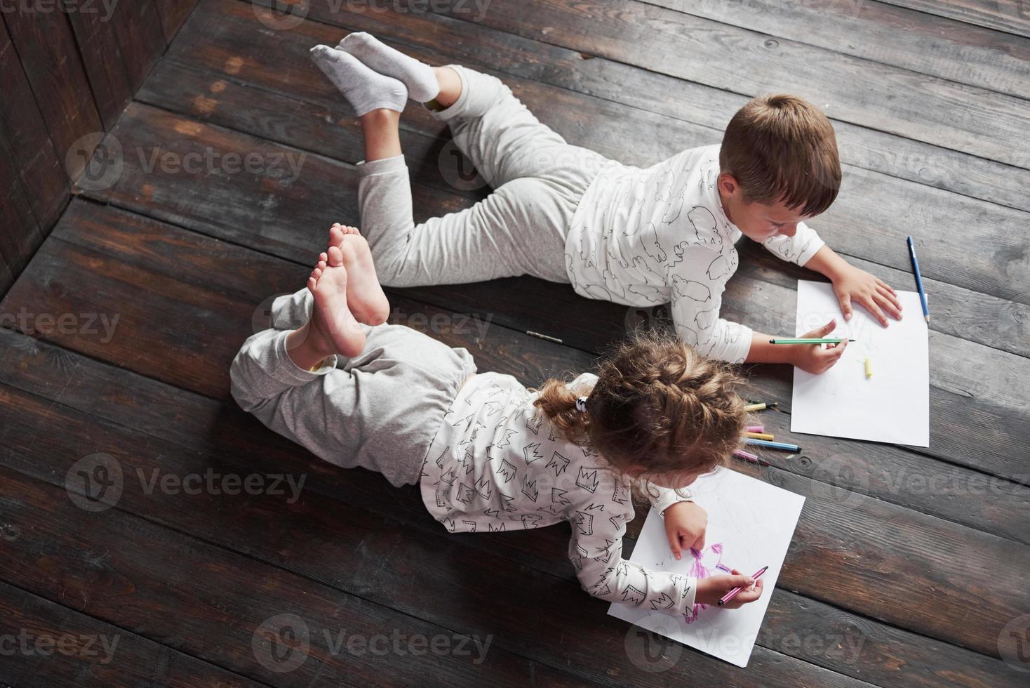 kinderen liggen in pyjama op de grond en tekenen met potloden. schattig kind schilderen met potloden foto