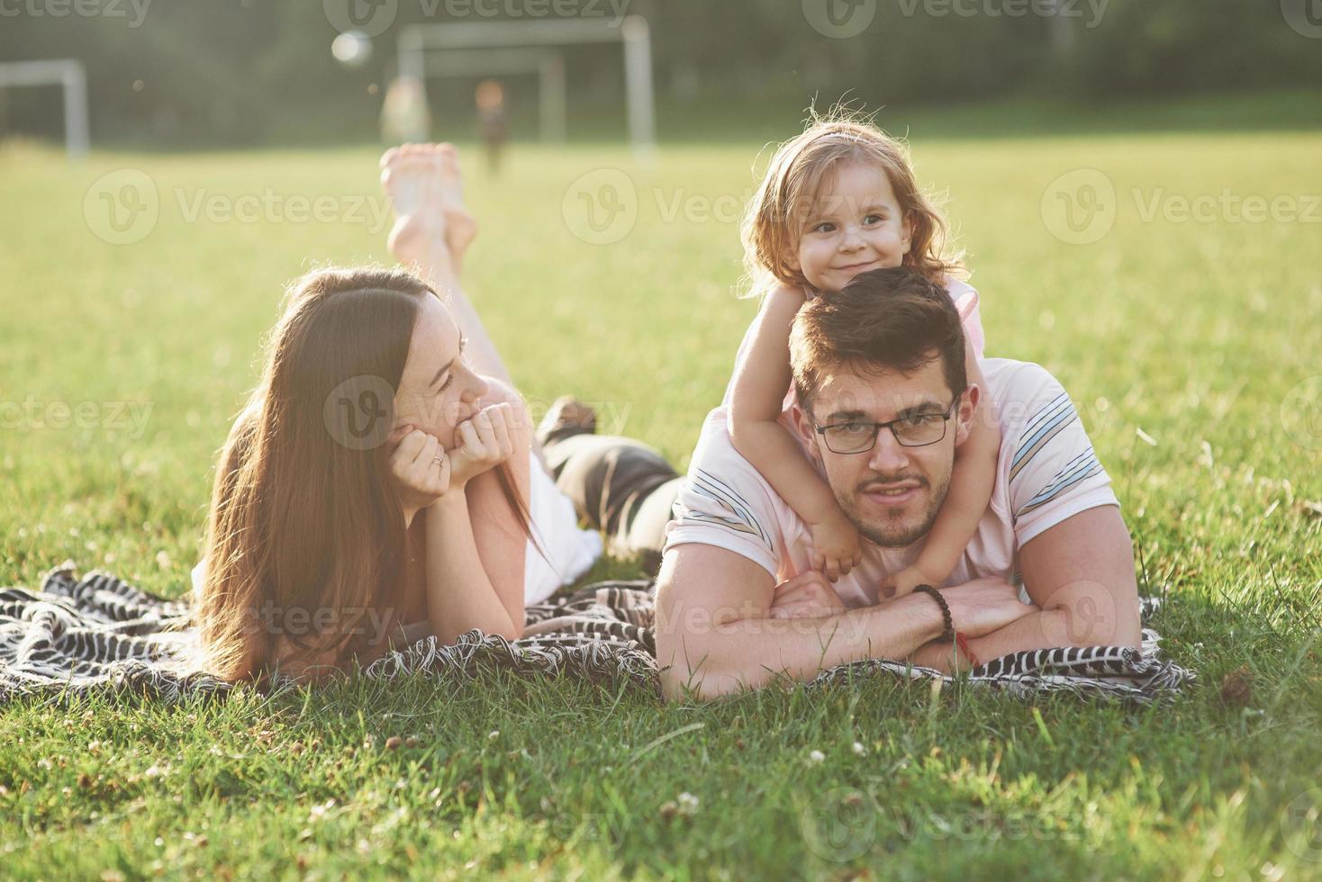 moeder en vader brengen gelukkig tijd samen door. dochtertje speelt met haar ouders buiten tijdens zonsondergang foto