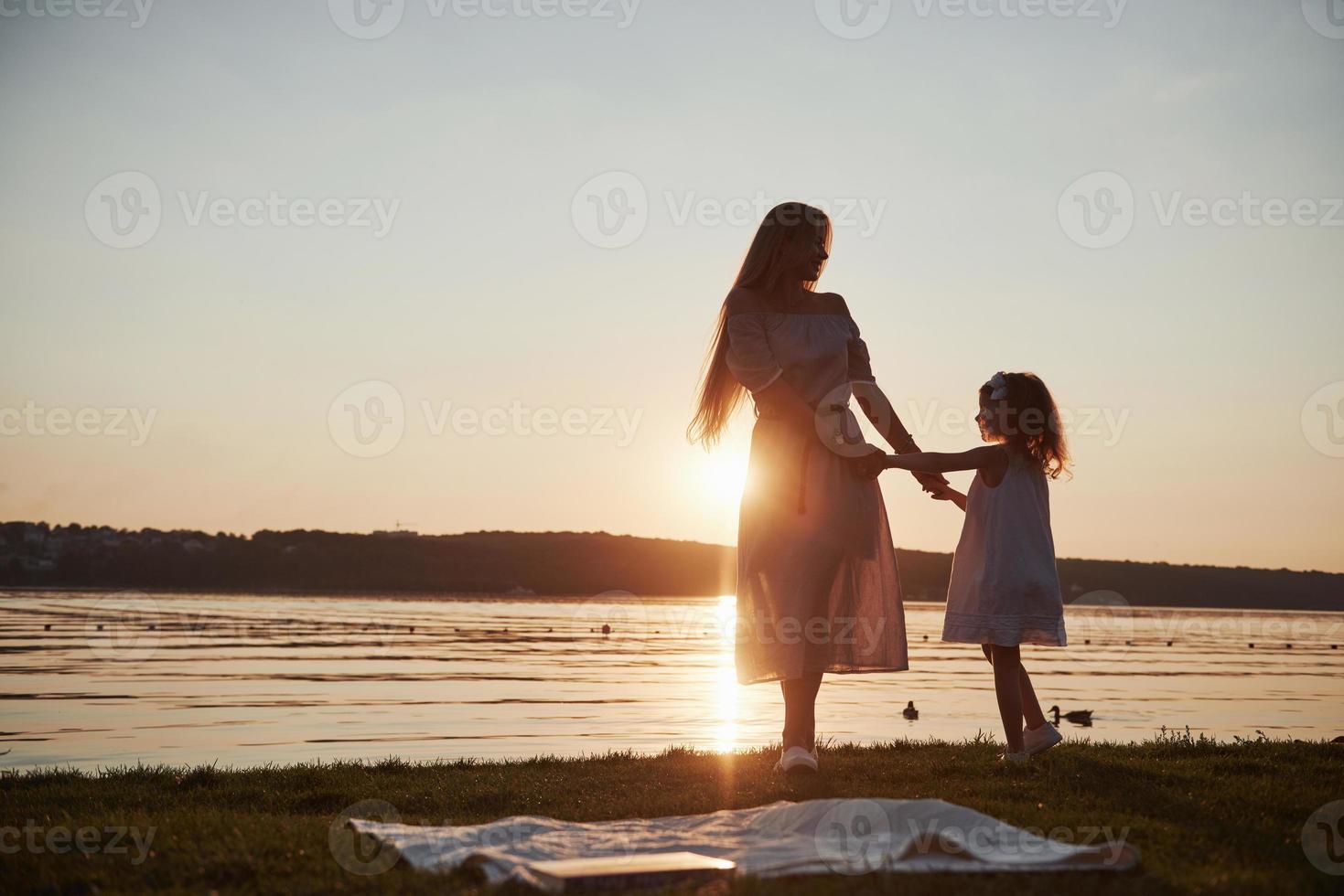 moeder speelt met haar baby op vakantie in de buurt van de oceaan, silhouetten bij zonsondergang foto