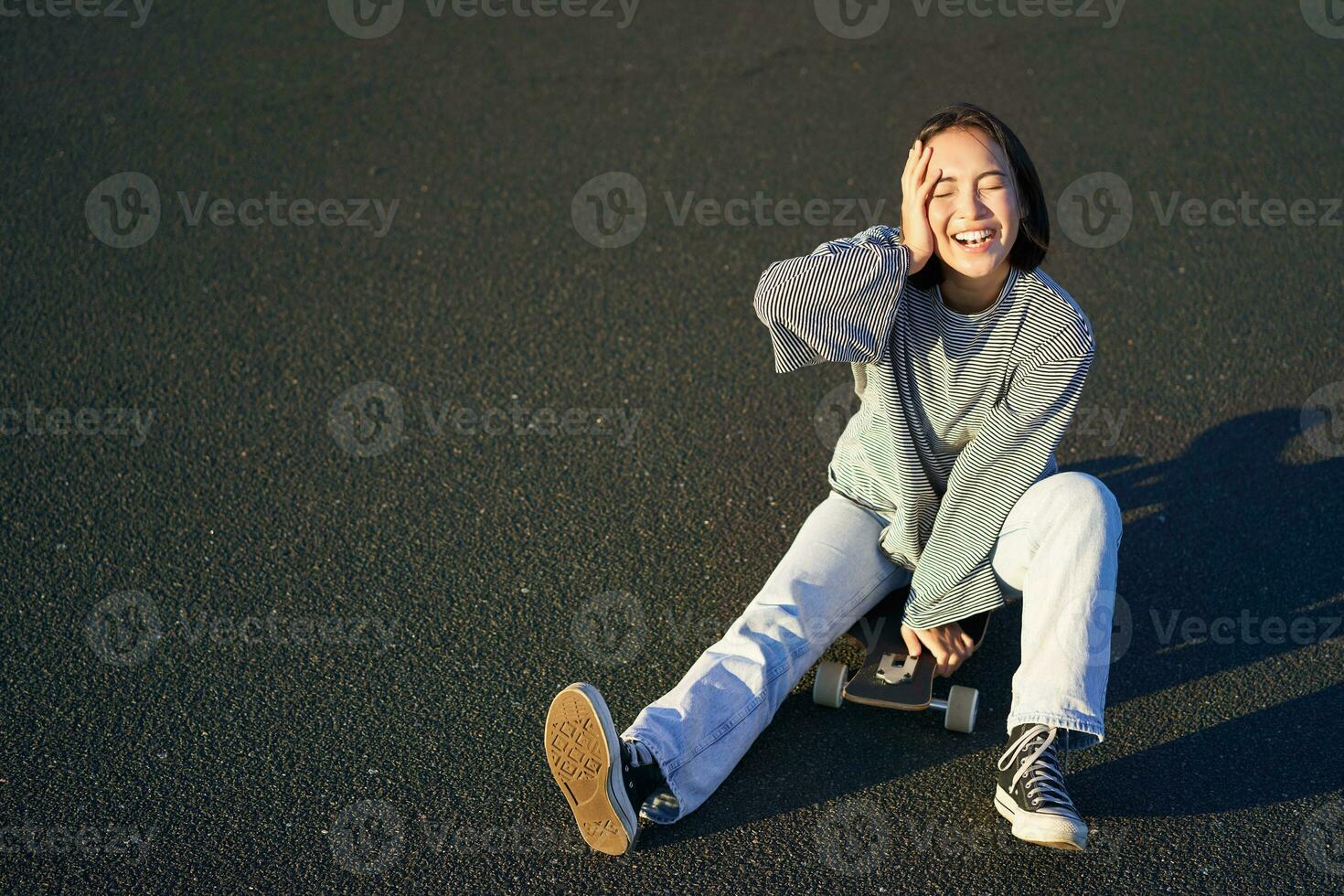 gelukkig mooi Koreaans tiener meisje zit Aan haar skateboard, cruisen Aan longboard, vervelend gewoontjes kleren foto