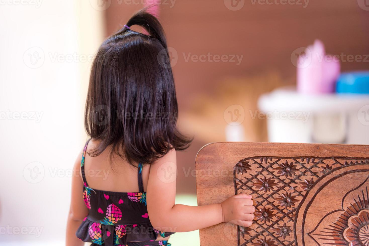 de achterkant van het Aziatische schattige meisje met schouderlang zwart haar. voor het huis stond een kind in een zwart badpak haar moeder op te wachten. kind is 3 jaar oud. foto