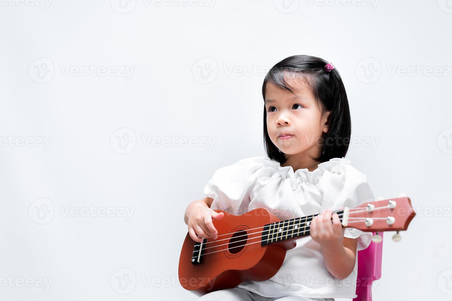 aziatisch schattig klein kind oefent om de ukelele te spelen. kinderen leren muziek in lessen. op studio witte achtergrond. foto