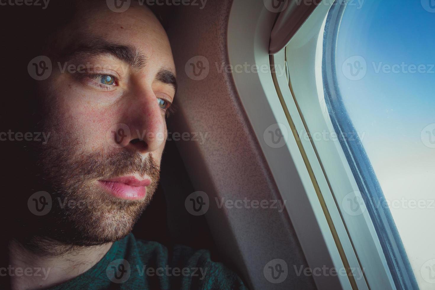 close-up van een peinzende man die door het raam van een vliegtuig naar buiten kijkt foto