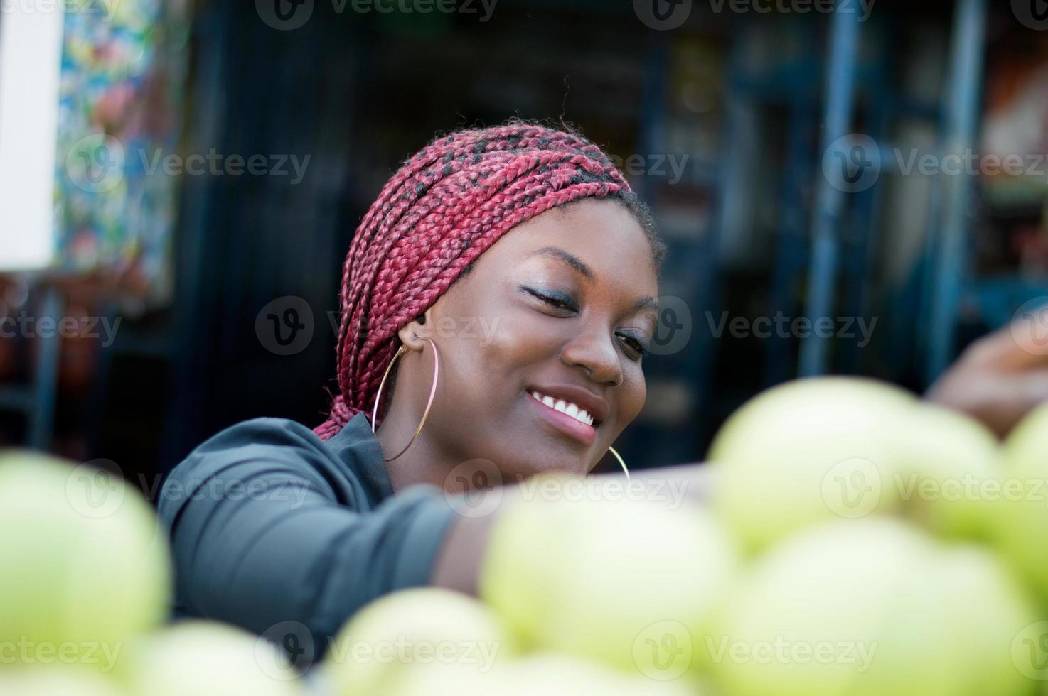 glimlachende jonge vrouw die appel kiest bij straatmarkt. foto