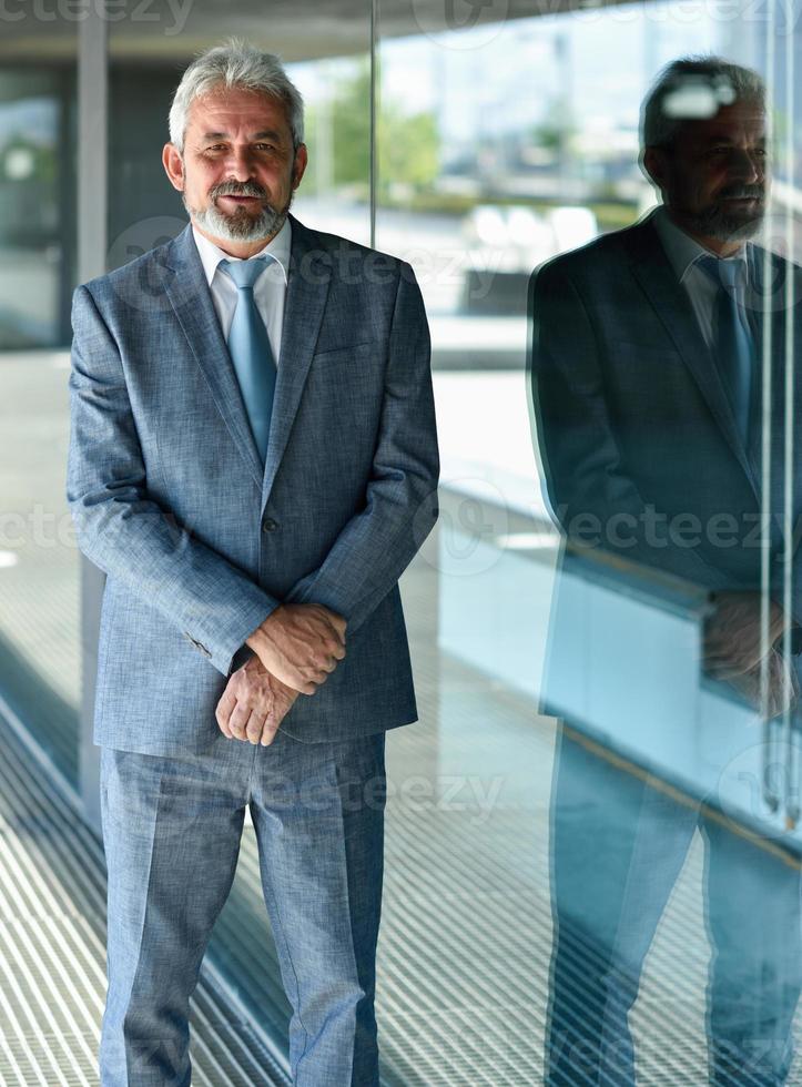 senior zakenman met armen gekruist buiten modern kantoorgebouw. foto