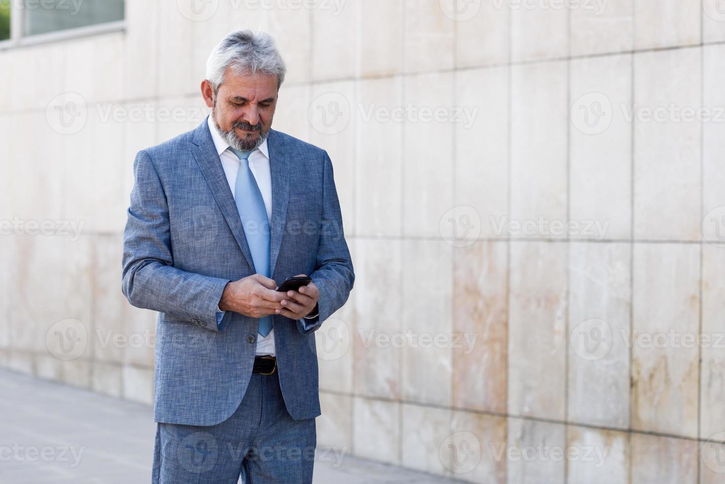 senior zakenman sms'en met smartphone buiten modern kantoorgebouw. foto