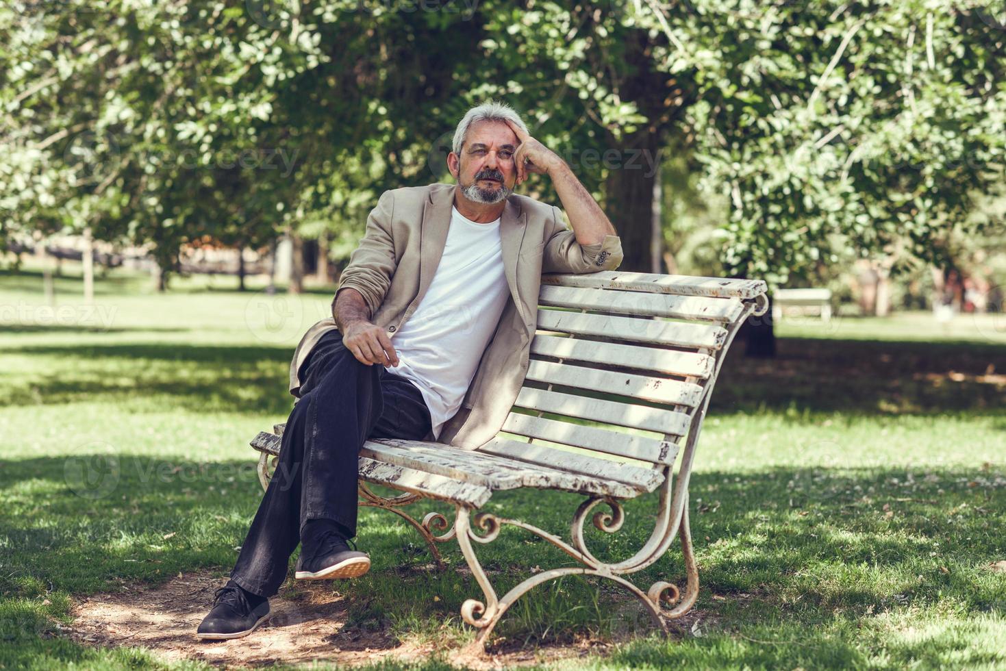 peinzende volwassen man zittend op een bankje in een stadspark. foto