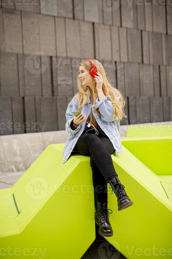 jonge vrouw luistert naar de muziek van de mobiele telefoon op een moderne openbare bank foto