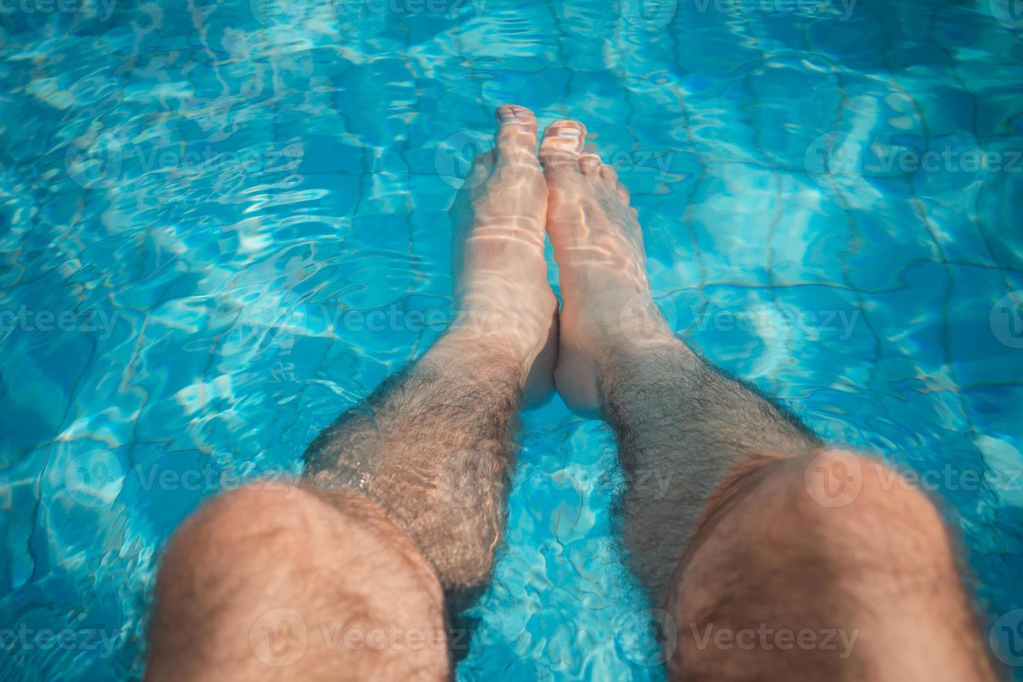 jonge man ontspanning bij het zwembad met zijn benen in het water foto