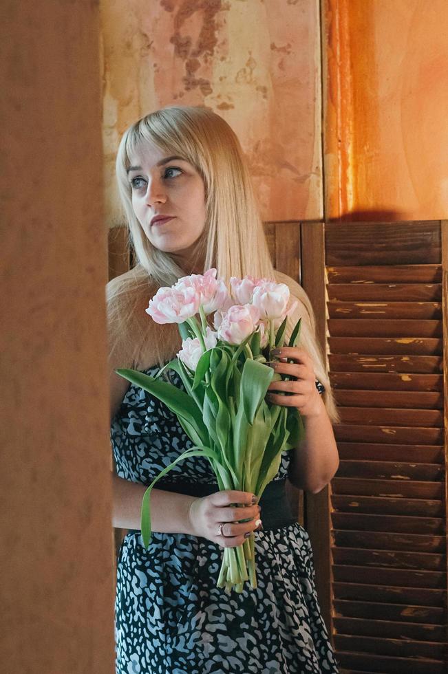 een blonde vrouw met boeket bloemen bij het raam foto