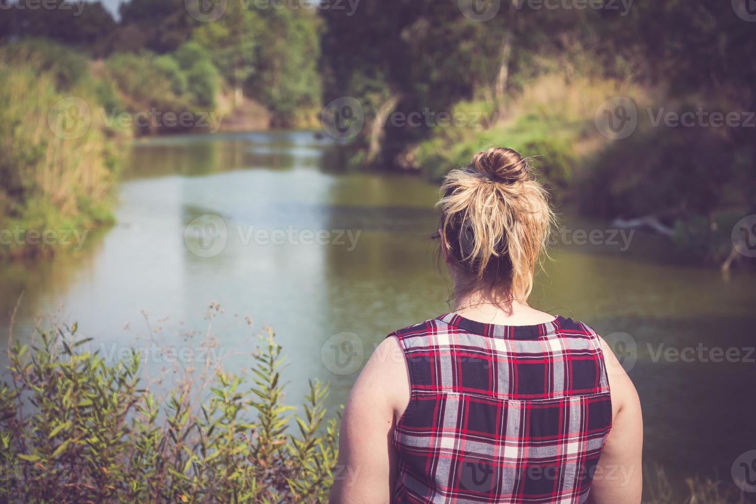 achteraanzicht van een vrouw die staat en wegkijkt naar de oevers van de rivier foto