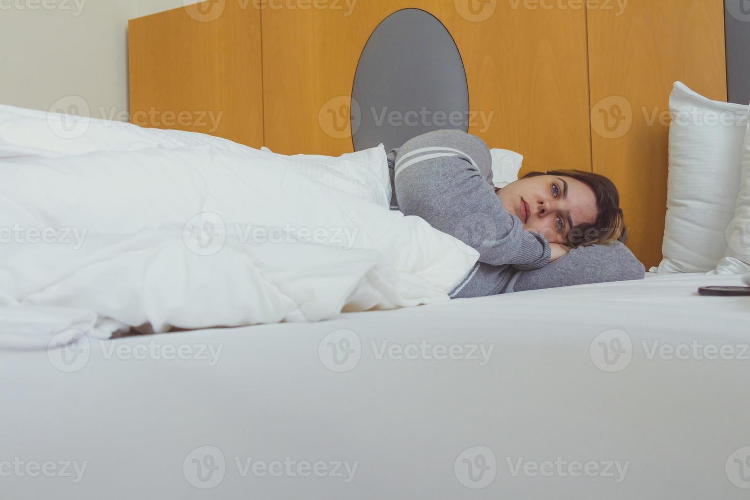 jonge vrouw dagdromen terwijl liggend op bed onder de deken foto