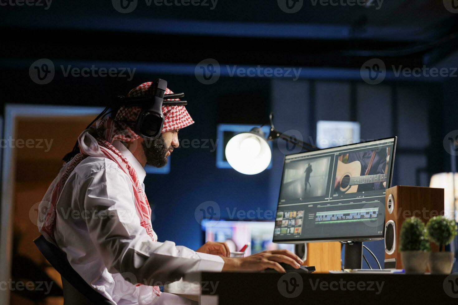 Arabisch vent regisseur za Bij tafel, aandachtig werken Aan film na-productie. moslim video editor in traditioneel gewaad onderzoekt beeldmateriaal Aan computer scherm terwijl vervelend draadloze koptelefoon. foto