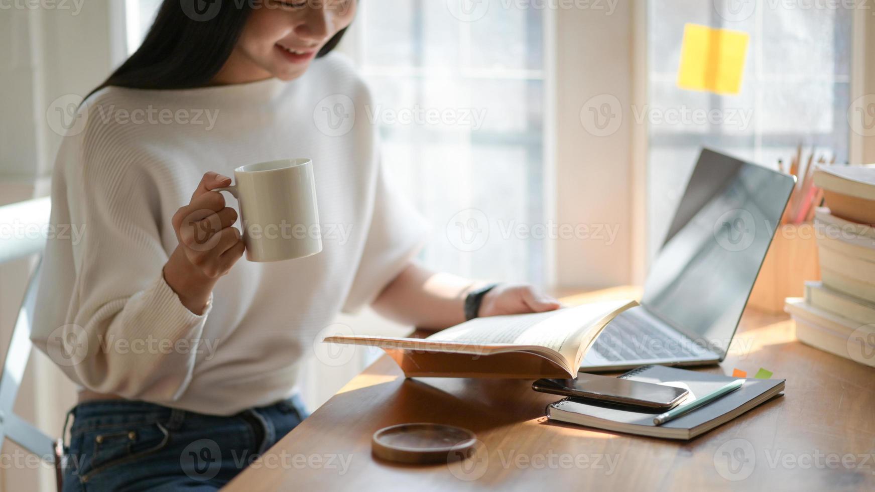 een foto van een jonge student die een kopje koffie vasthoudt en leest in een mooi licht café.