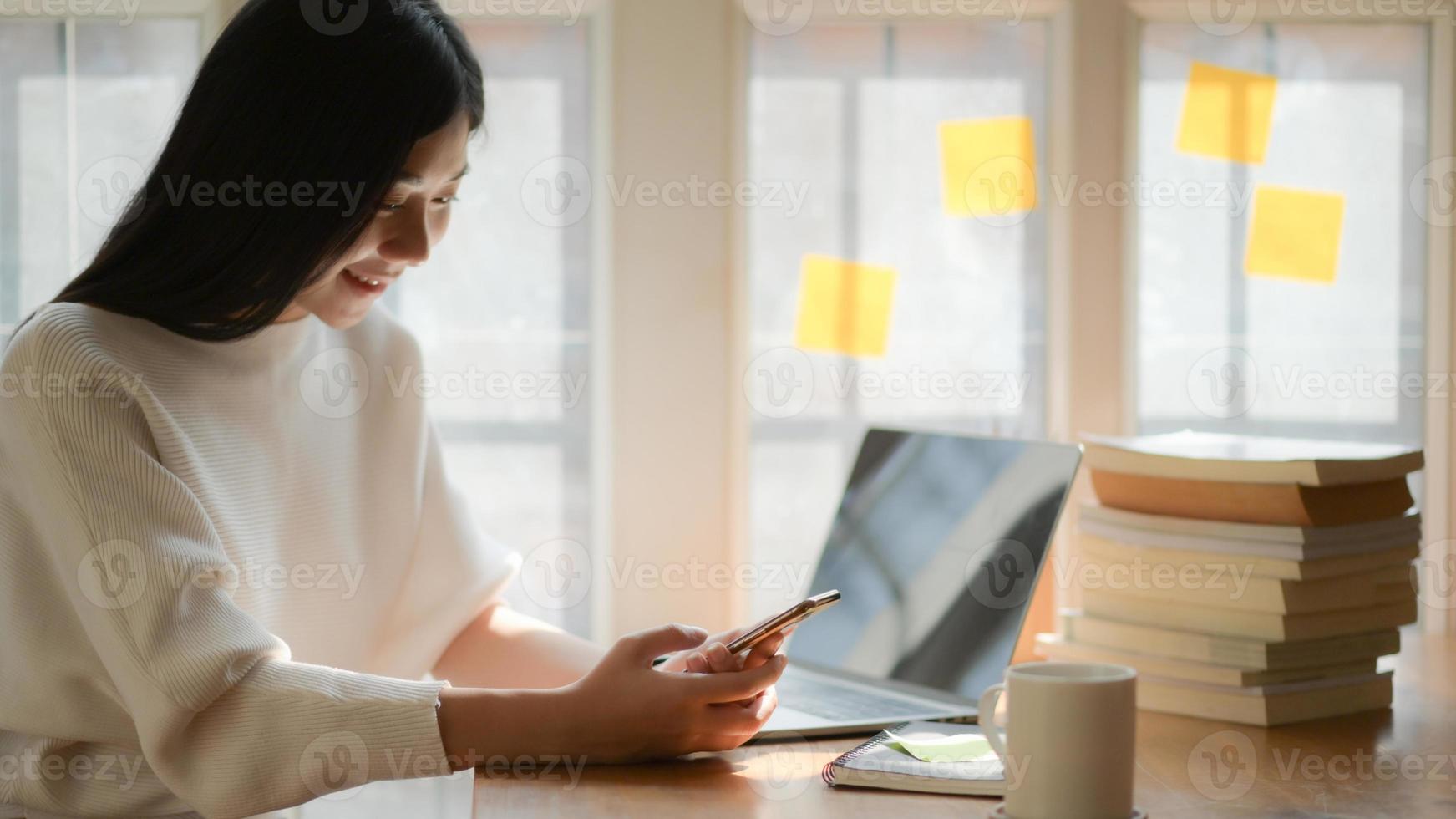 een jonge vrouwelijke student gebruikt een smartphone om te chatten met vrienden met een lachend gezicht. ze rustte tijdens het lezen van het examen. foto