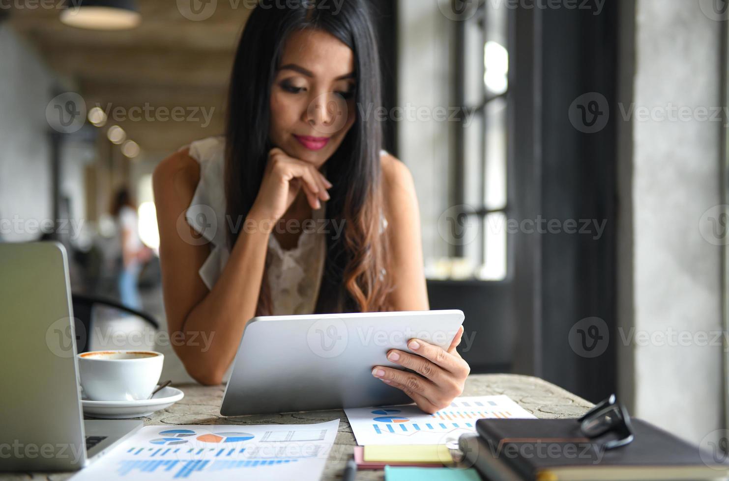 vrouwelijke zakenlieden gebruiken de tablet tijdens hun vrije tijd. ze lacht blij. grafieken, documenten op tafel gelegd. foto