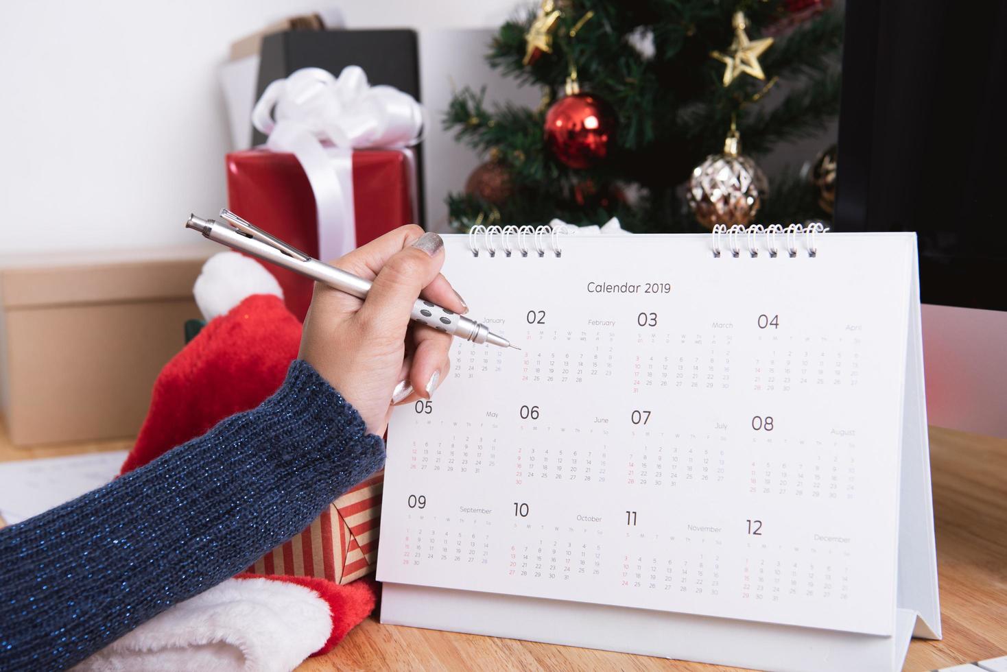 zakenvrouw kalenderplanner schrijven in kerstvakantie op kantoor met kerstversiering op tafel. foto