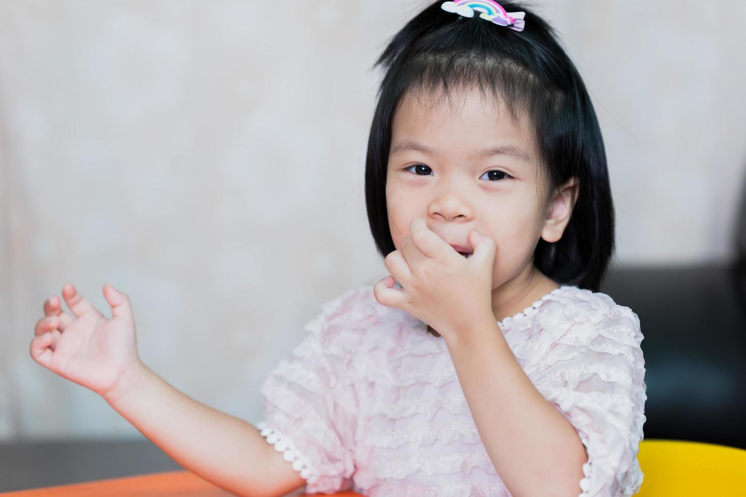 een schattig klein meisje krabt aan haar lippen van jeuk. kinderen glimlachen stiekem. foto