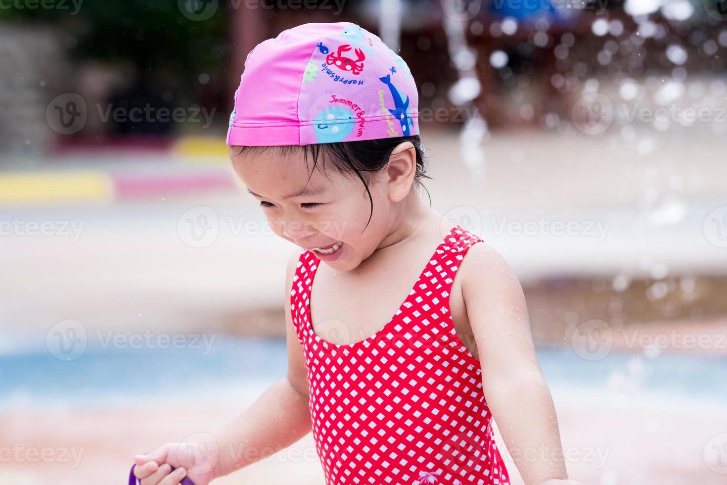 portret van gelukkig schattig meisje water spelen. kind dat rood zwempak en roze zwemhoed draagt. lieve lach kind het is leuk. in de zomer. foto