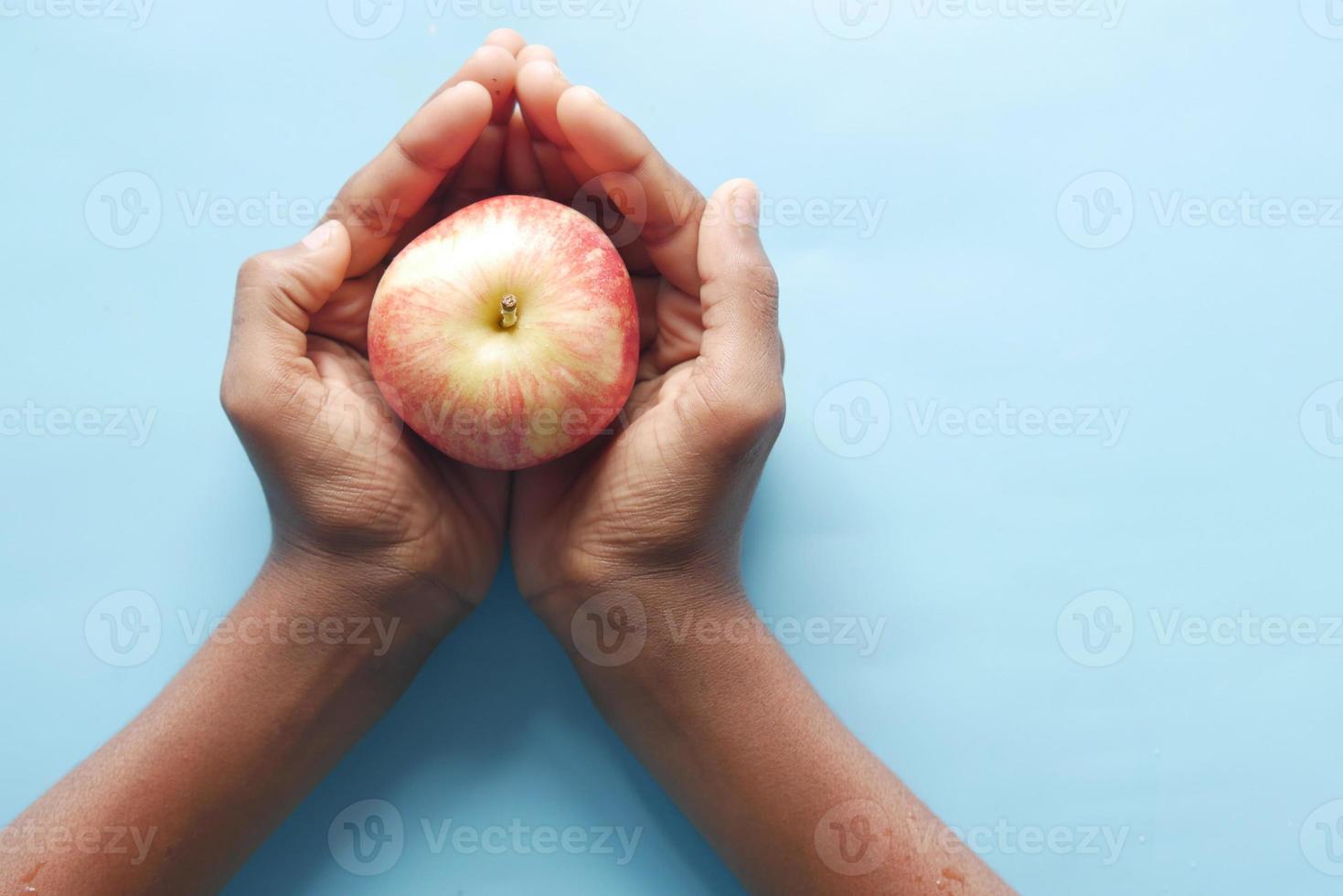 kind jongen hand houdt een appel op blauwe achtergrond foto
