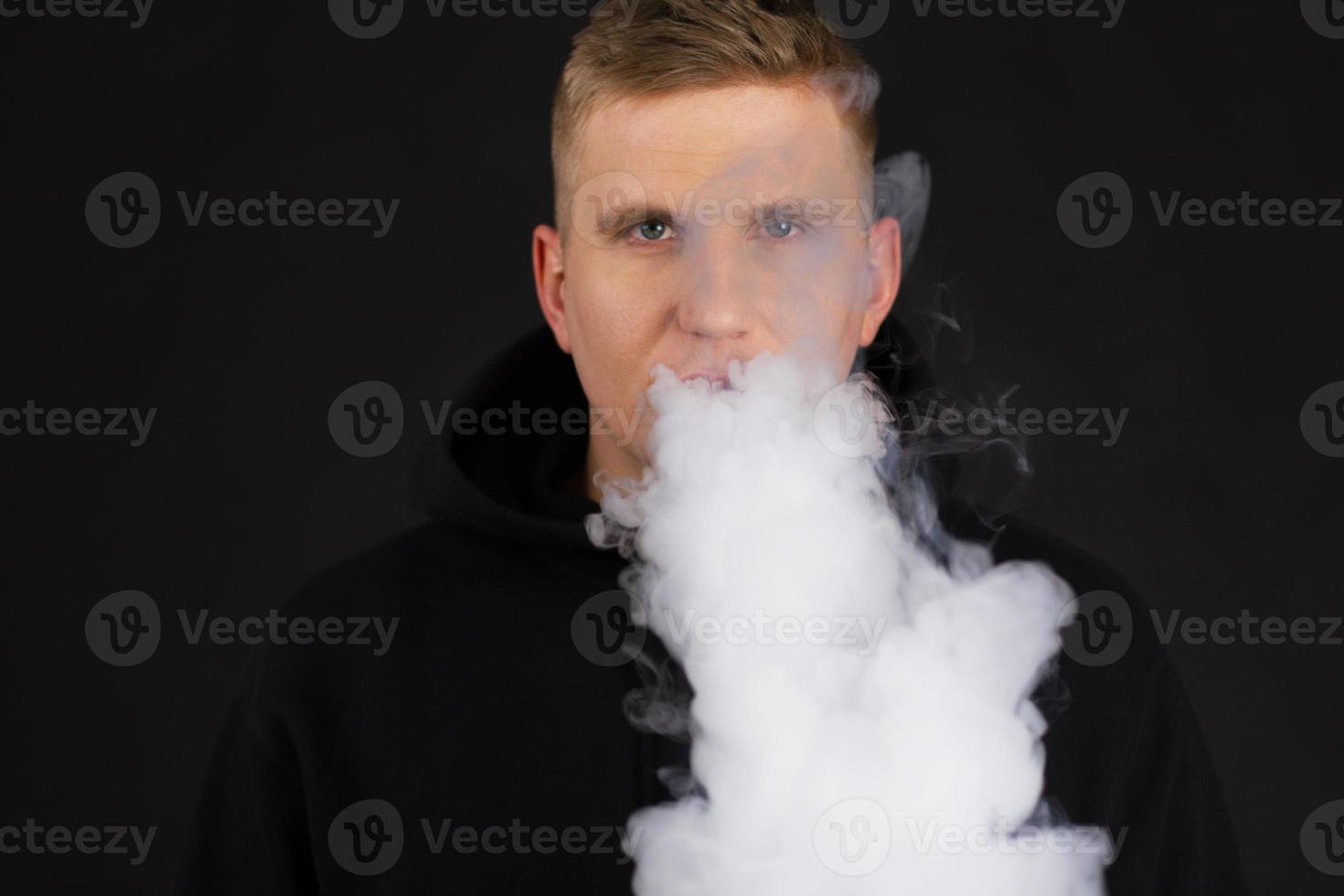 mannen roken een elektronische sigaret op de donkere achtergrond. selectieve focus foto