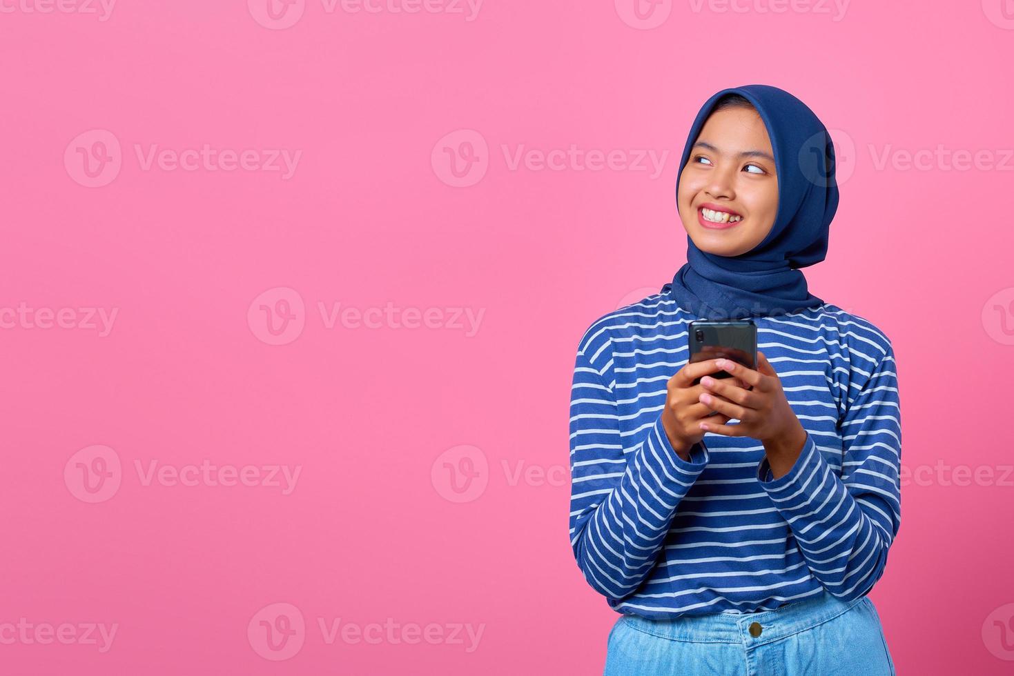 portret van glimlachende jonge aziatische vrouw die mobiele telefoon vasthoudt en opzij kijkt foto