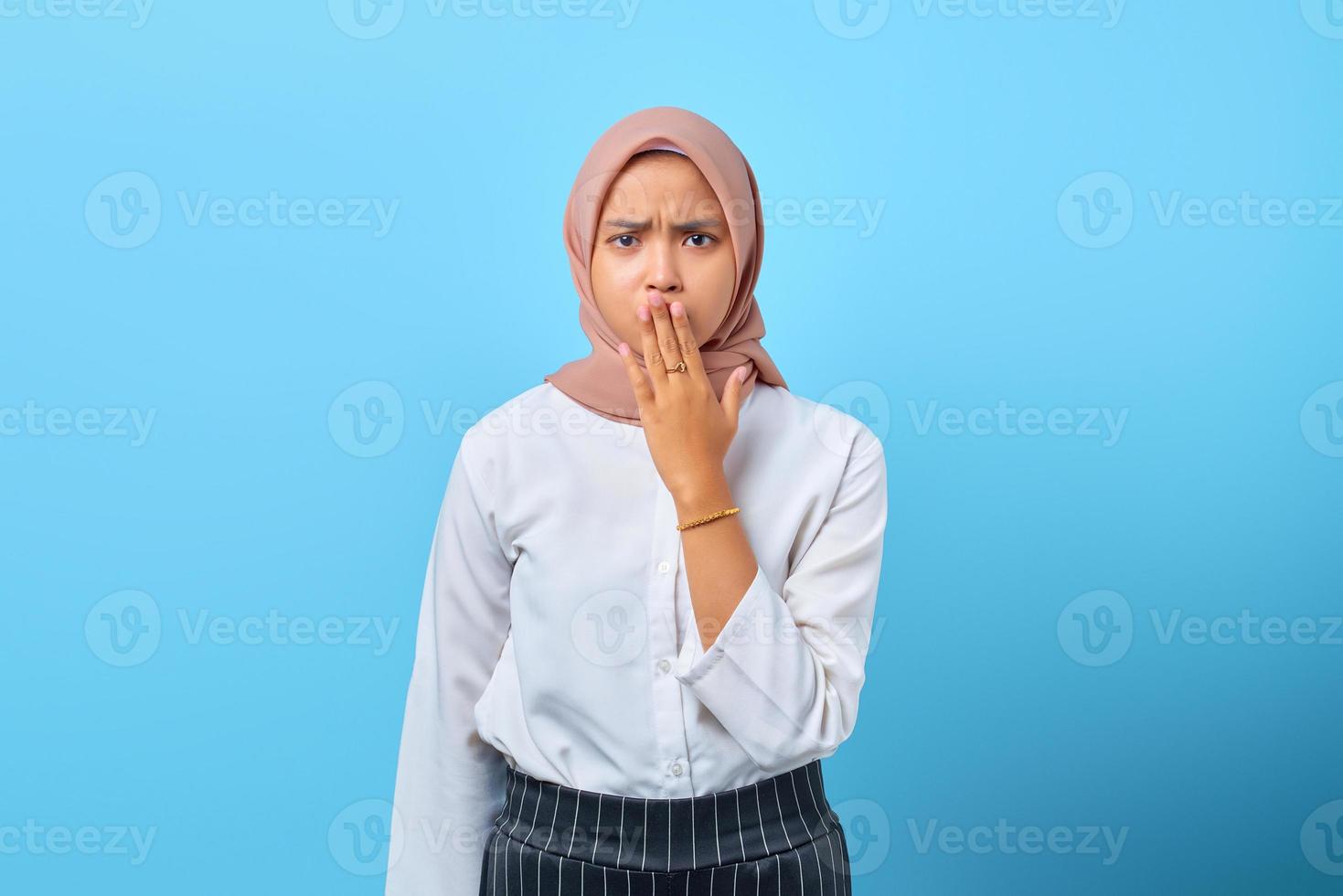 portret van verraste jonge aziatische vrouw die mond bedekt met handen over blauwe achtergrond foto