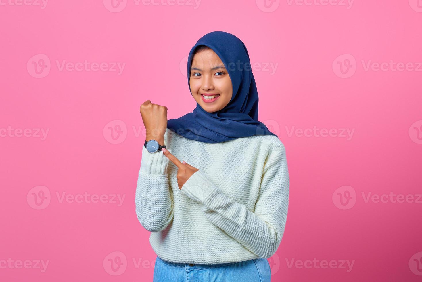 portret van glimlachende jonge aziatische vrouw die polshorloge met vinger toont en richt foto