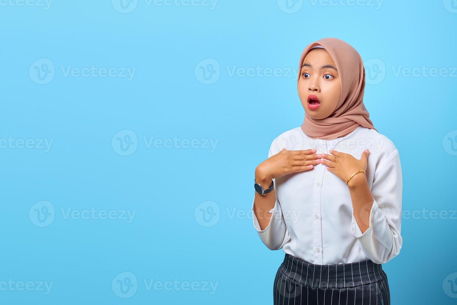 portret van geschokte jonge aziatische vrouw met open mond en hand op de borst over blauwe achtergrond foto