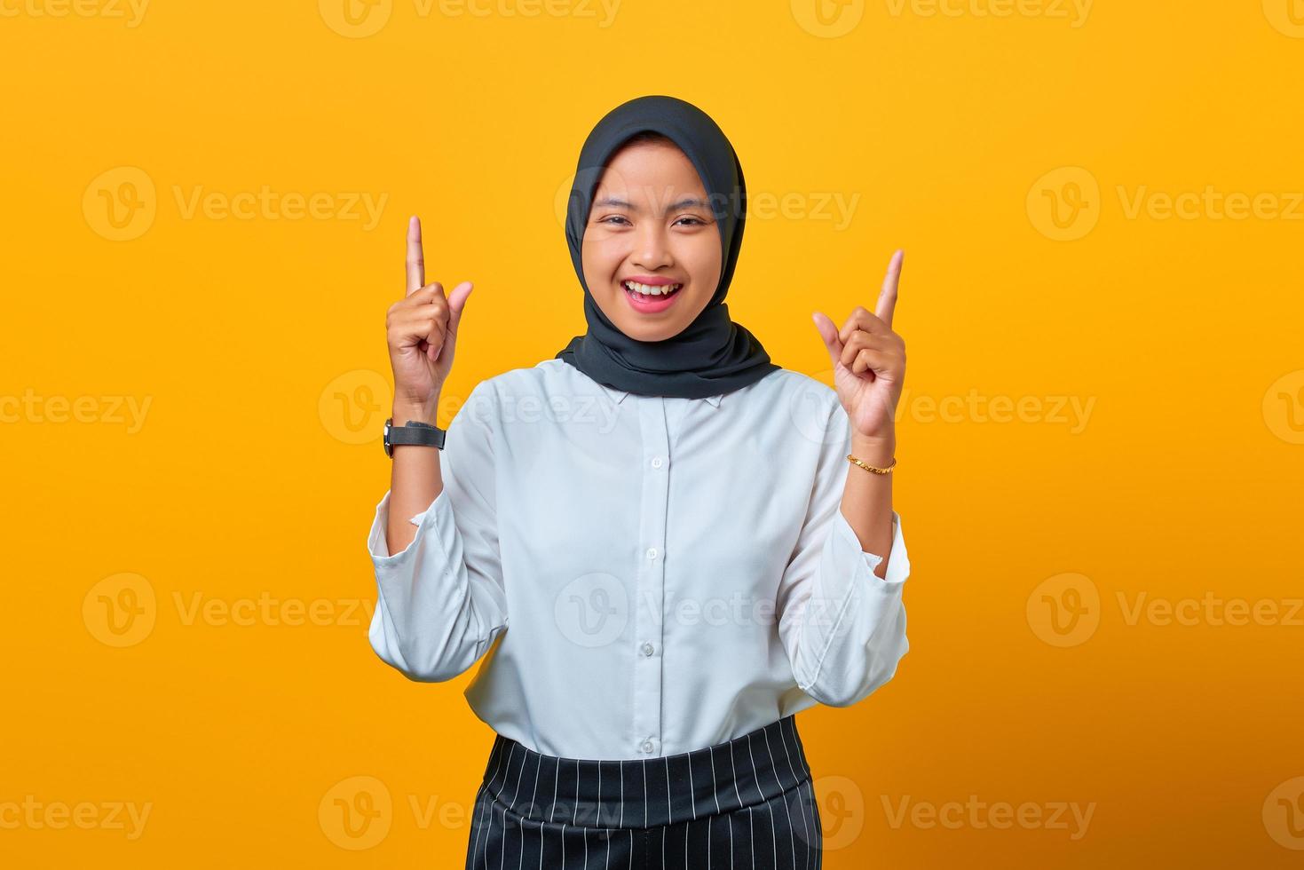 vrolijke jonge aziatische vrouw die naar boven wijst, geïsoleerd over gele achtergrond foto