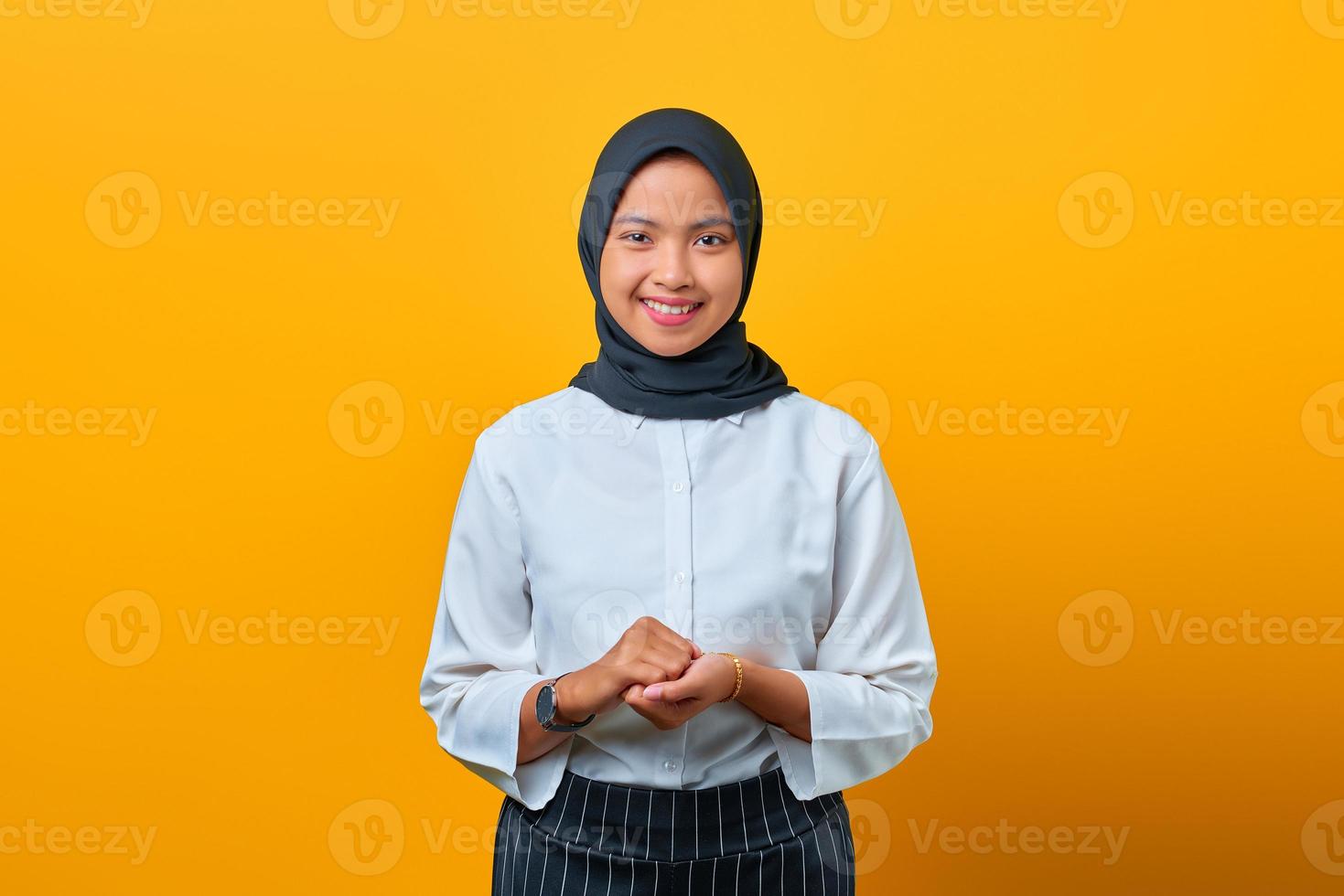 portret van gelukkige jonge aziatische vrouw houdt handen bij elkaar op gele achtergrond foto