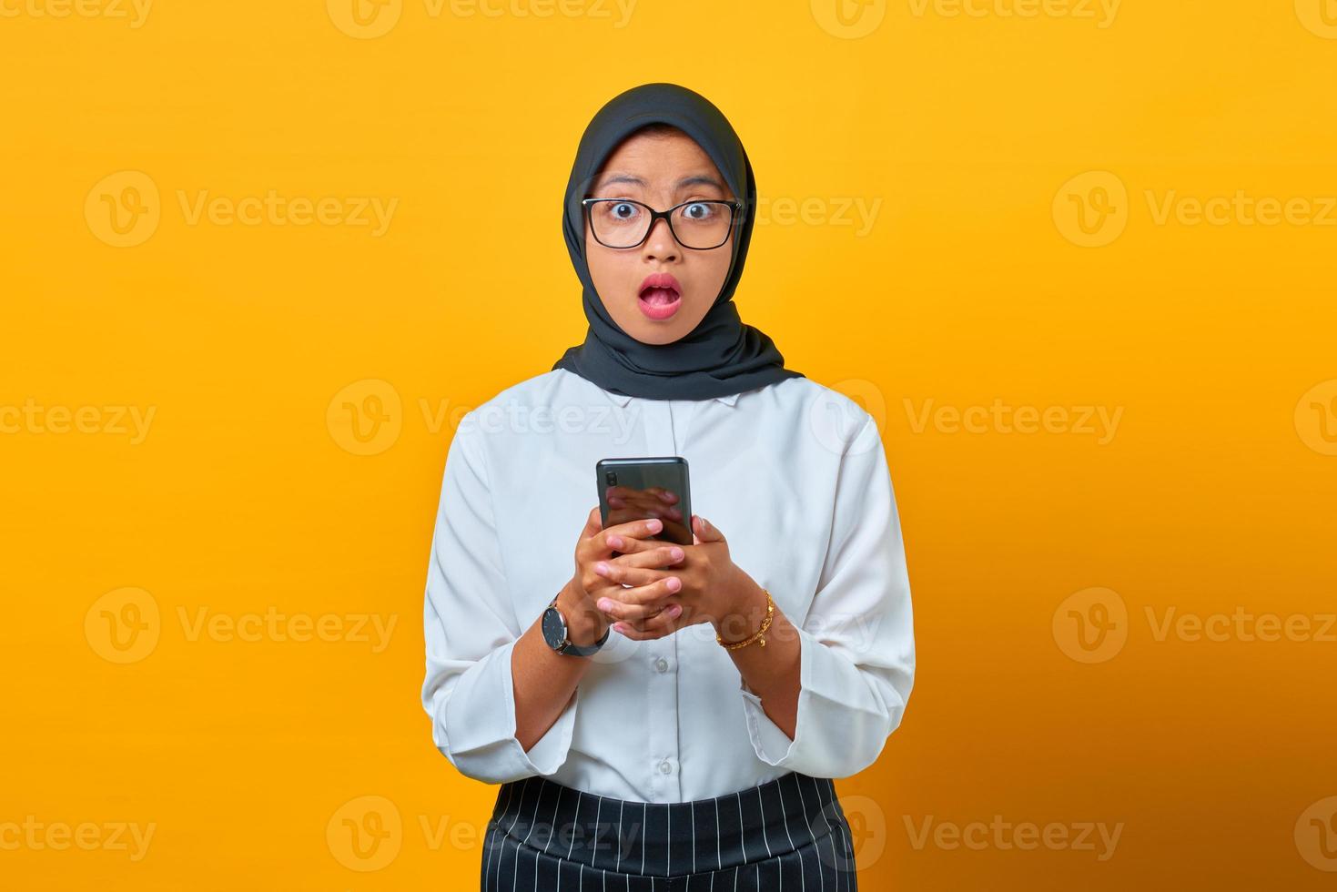 verraste jonge aziatische vrouw met mobiele telefoon met open mond op gele achtergrond foto