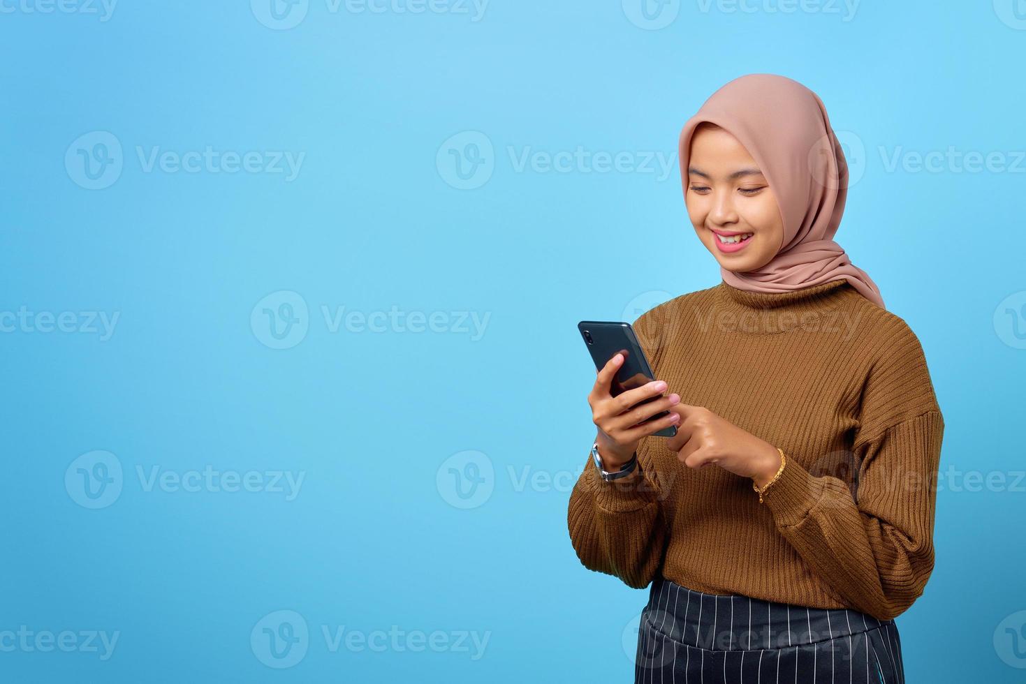 gelukkige jonge aziatische vrouw die een mobiele telefoon gebruikt en het smartphonescherm op blauwe achtergrond kijkt foto