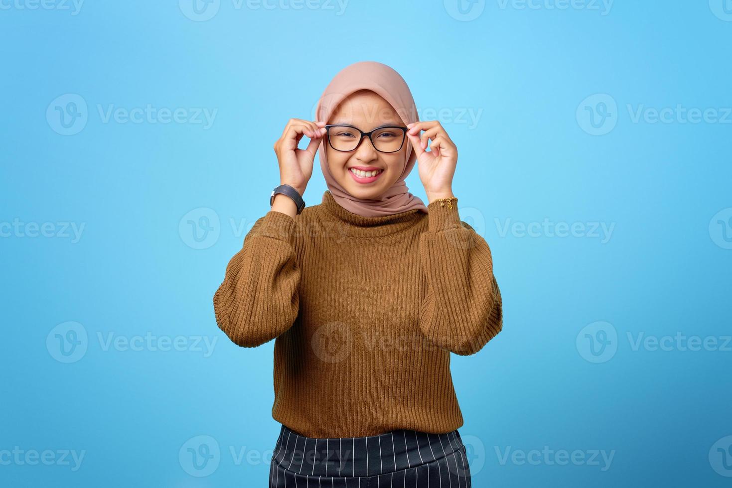 gelukkige jonge Aziatische vrouw hand op bril met lachende uitdrukking op blauwe achtergrond foto