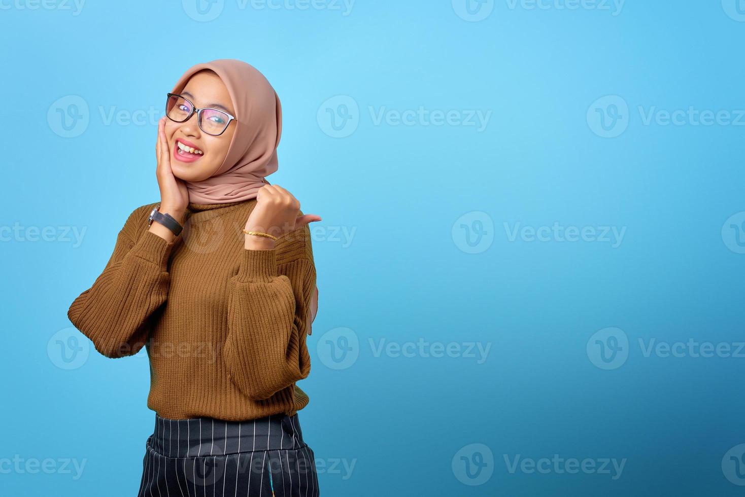 vrolijke jonge aziatische vrouw die met de vingers wijst naar kopieerruimte op blauwe achtergrond foto