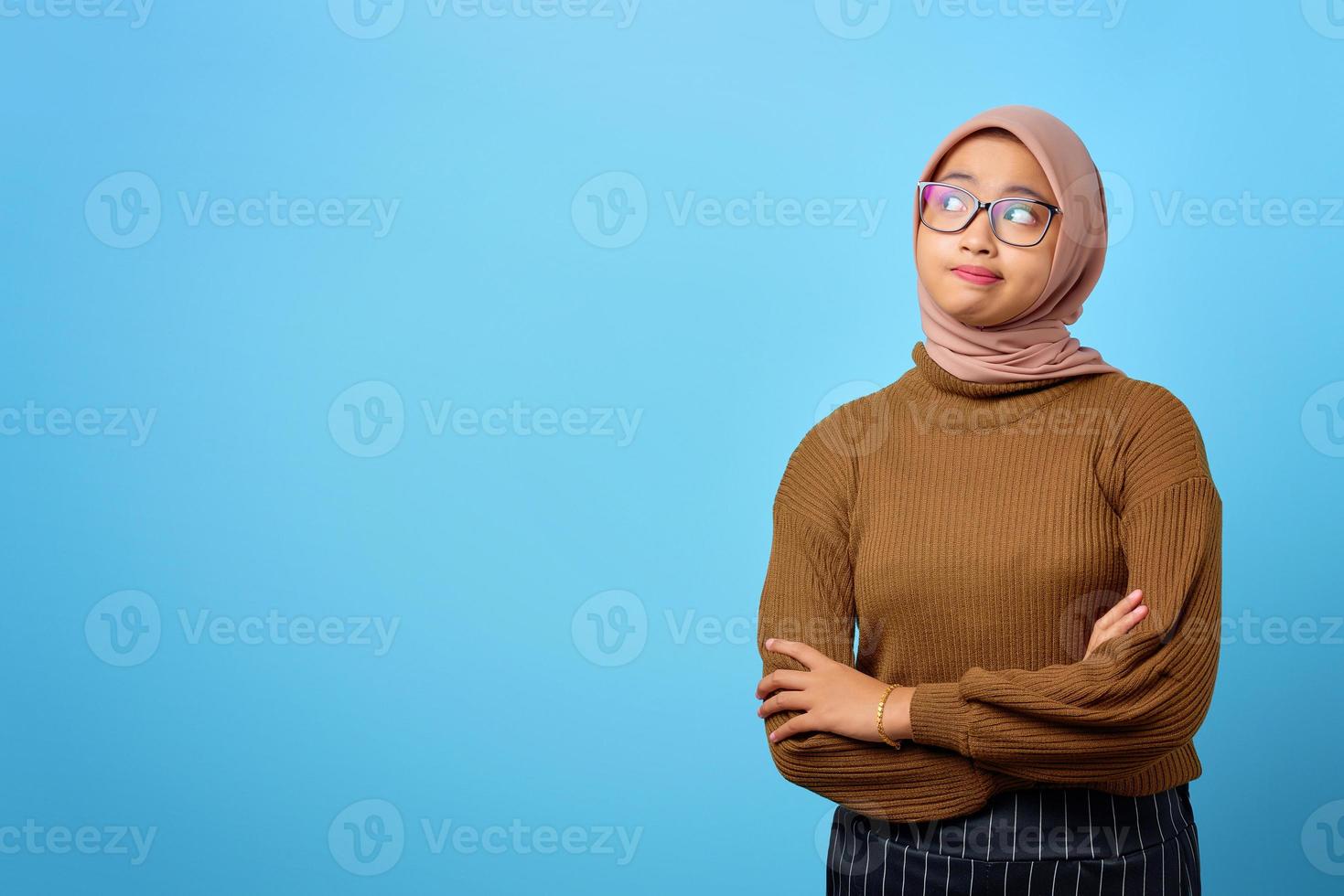 aantrekkelijke jonge aziatische vrouw die de arm kruist en zijwaarts kijkt op een blauwe achtergrond foto