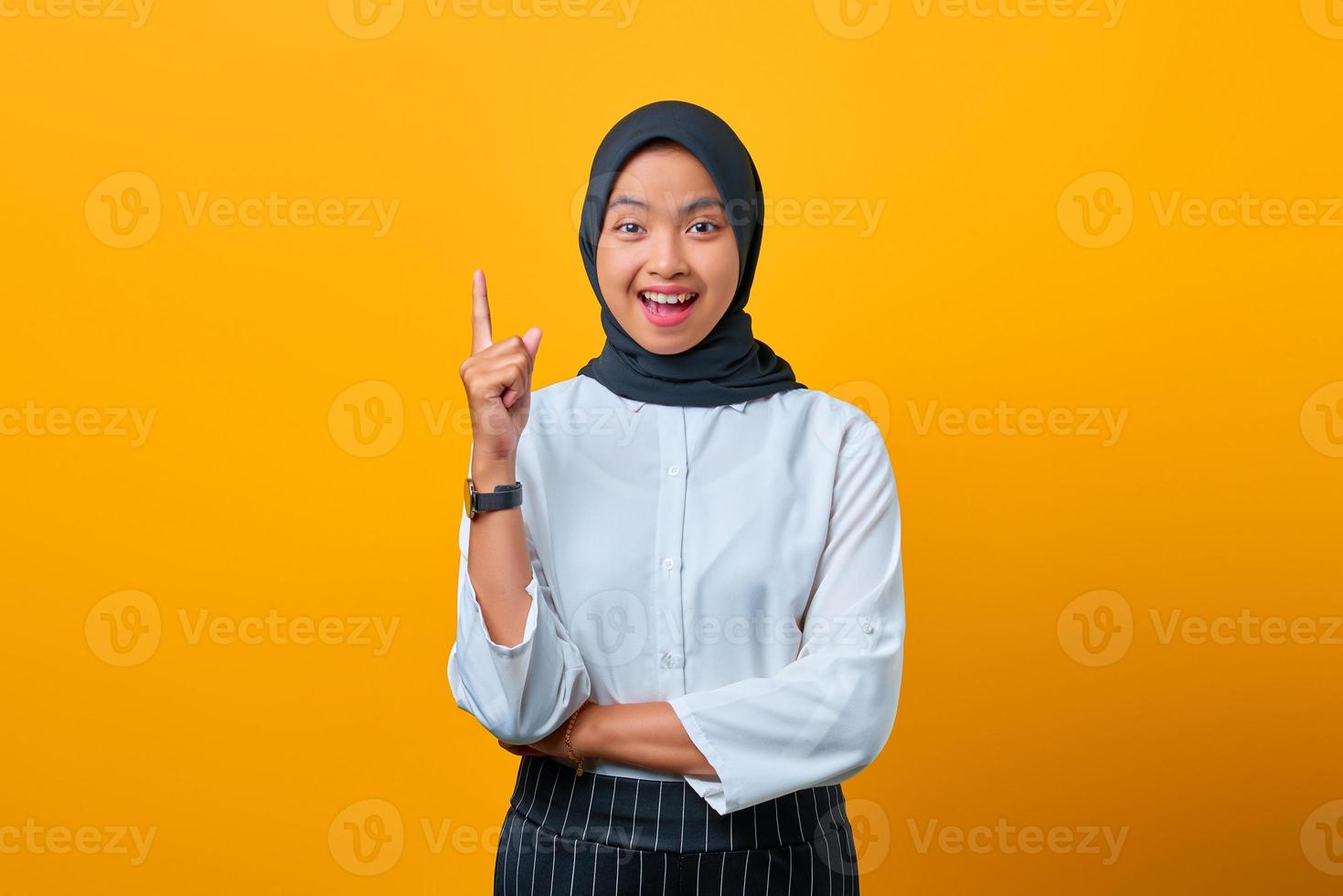 opgewonden mooie aziatische vrouw die wijsvinger opsteekt en idee op gele achtergrond zegt foto
