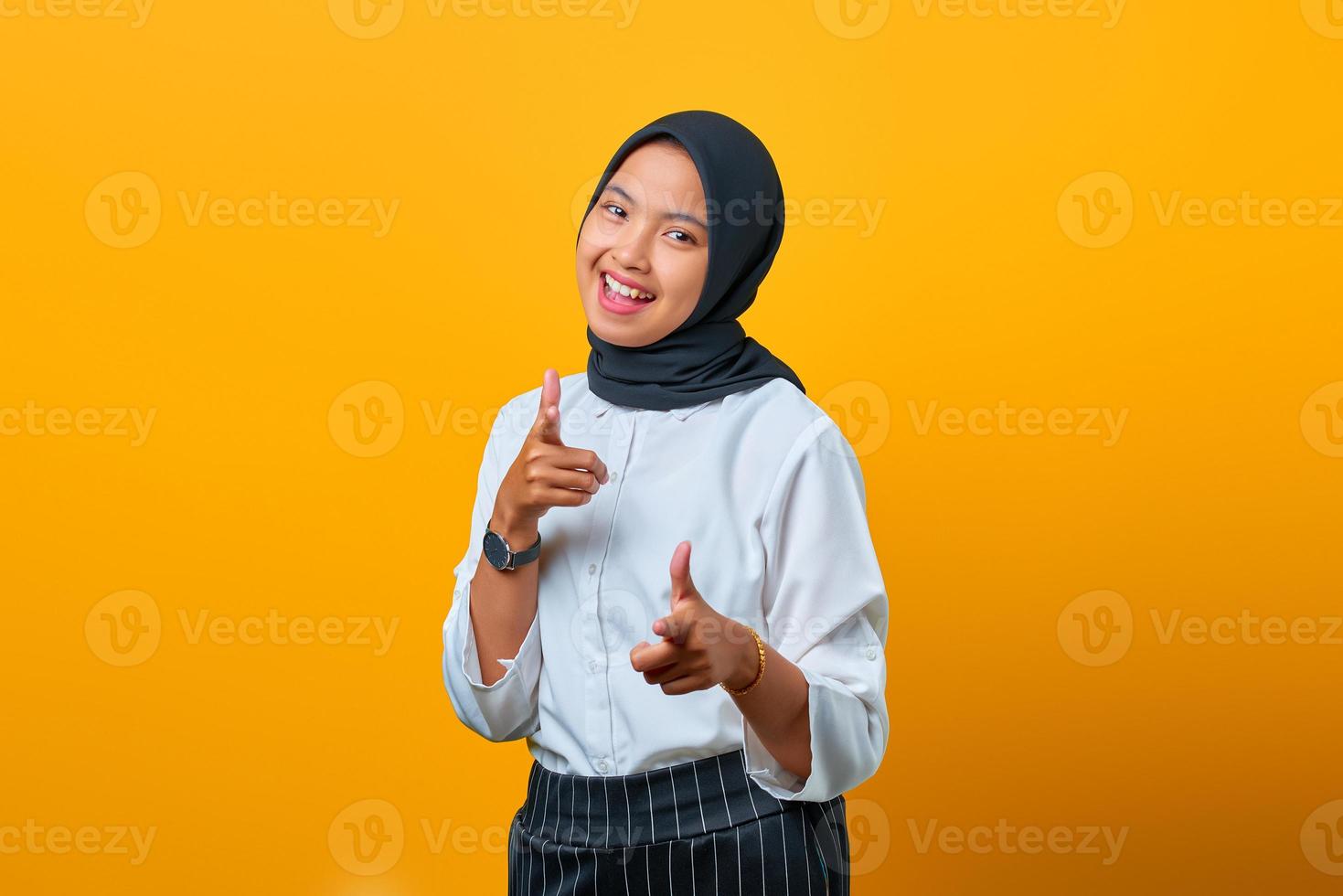 portret van glimlachende jonge aziatische vrouw die met de vingers naar de camera wijst op gele achtergrond foto