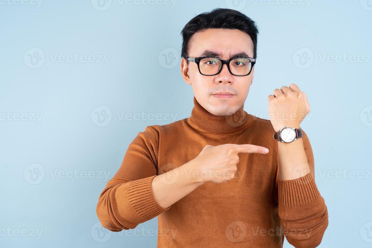 Aziatische man die zijn horloge op blauwe achtergrond kijkt foto