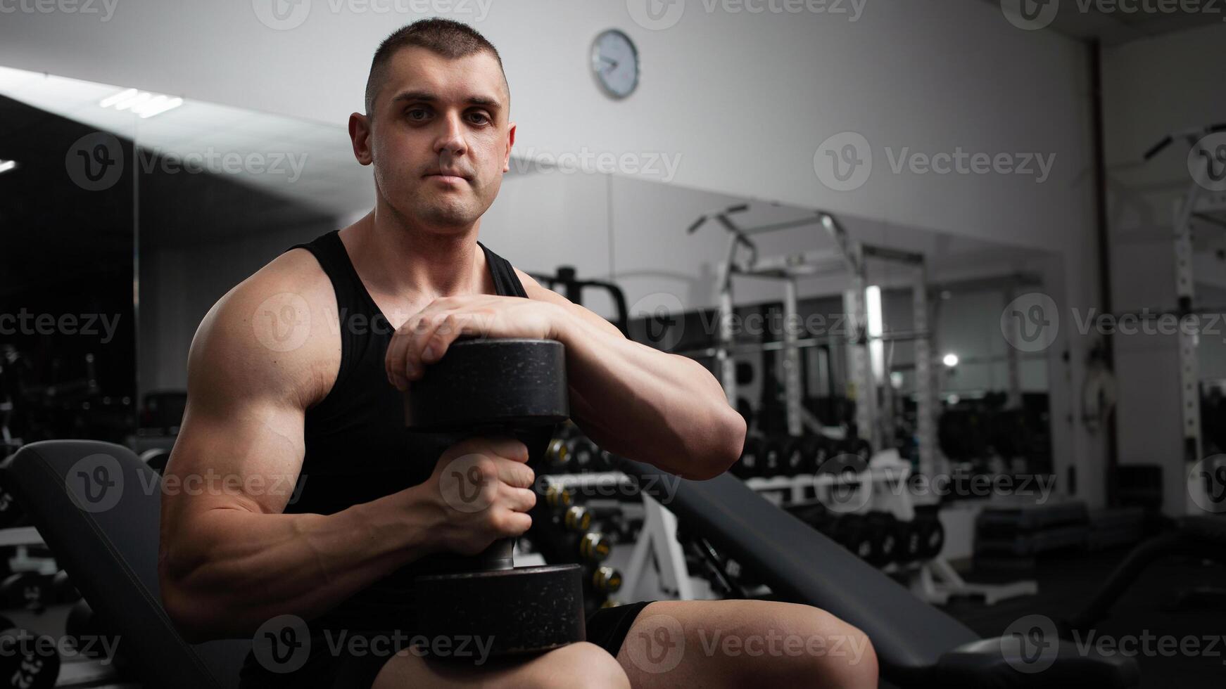 Mens presteert een oefening met halters Aan een simulator in de Sportschool. atleet, bodybuilder, geschiktheid coach. gespierd sexy lichaam. looks in de camera foto