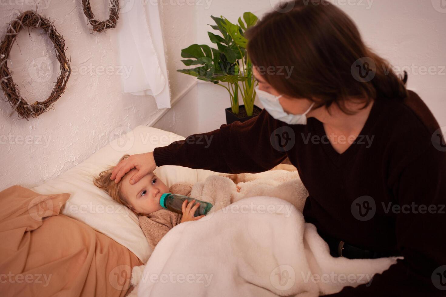 de kind is ziek, de vader in een masker cheques de temperatuur van zijn dochter. influenza, koud, coronavirus, covid, huis quarantaine. de kind is ziek en leugens Aan de bed, de Mens is nemen zorg foto