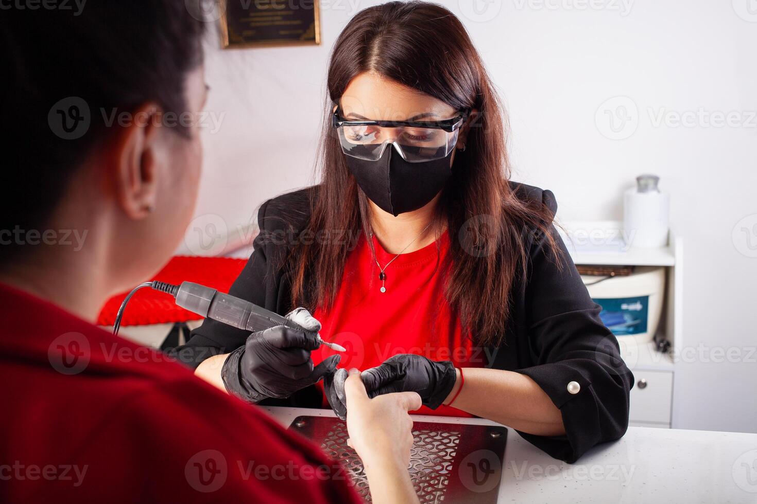 de manicure houdt handen van de cliënt in schoonheid salon Aan bureaublad voor manicure met nagel poetsmiddelen, servetten, crèmes en verlichting instrumenten foto