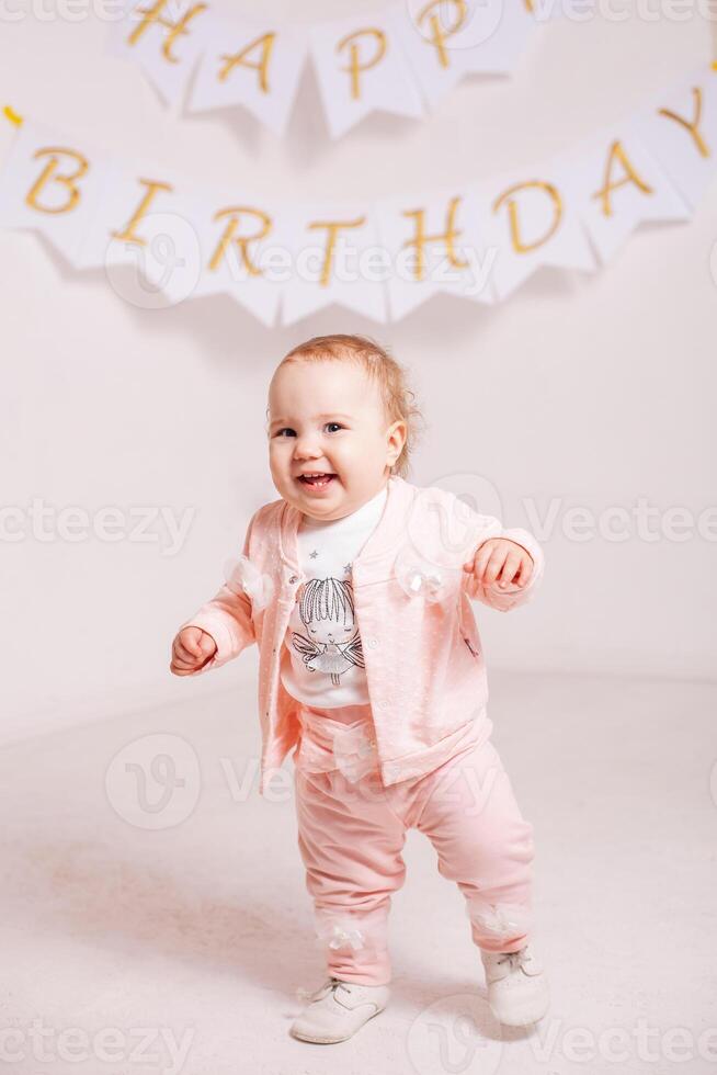 een weinig meisje in een roze pak Aan een wit achtergrond viert haar verjaardag foto
