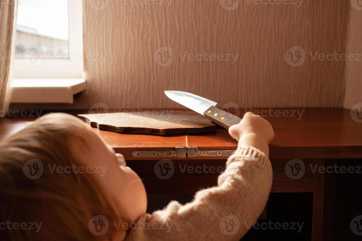 de kind trekt een mes van de tafel. de kind kan snee, kinderen huis gevaren. een weinig een jaar oud meisje met een mes. foto