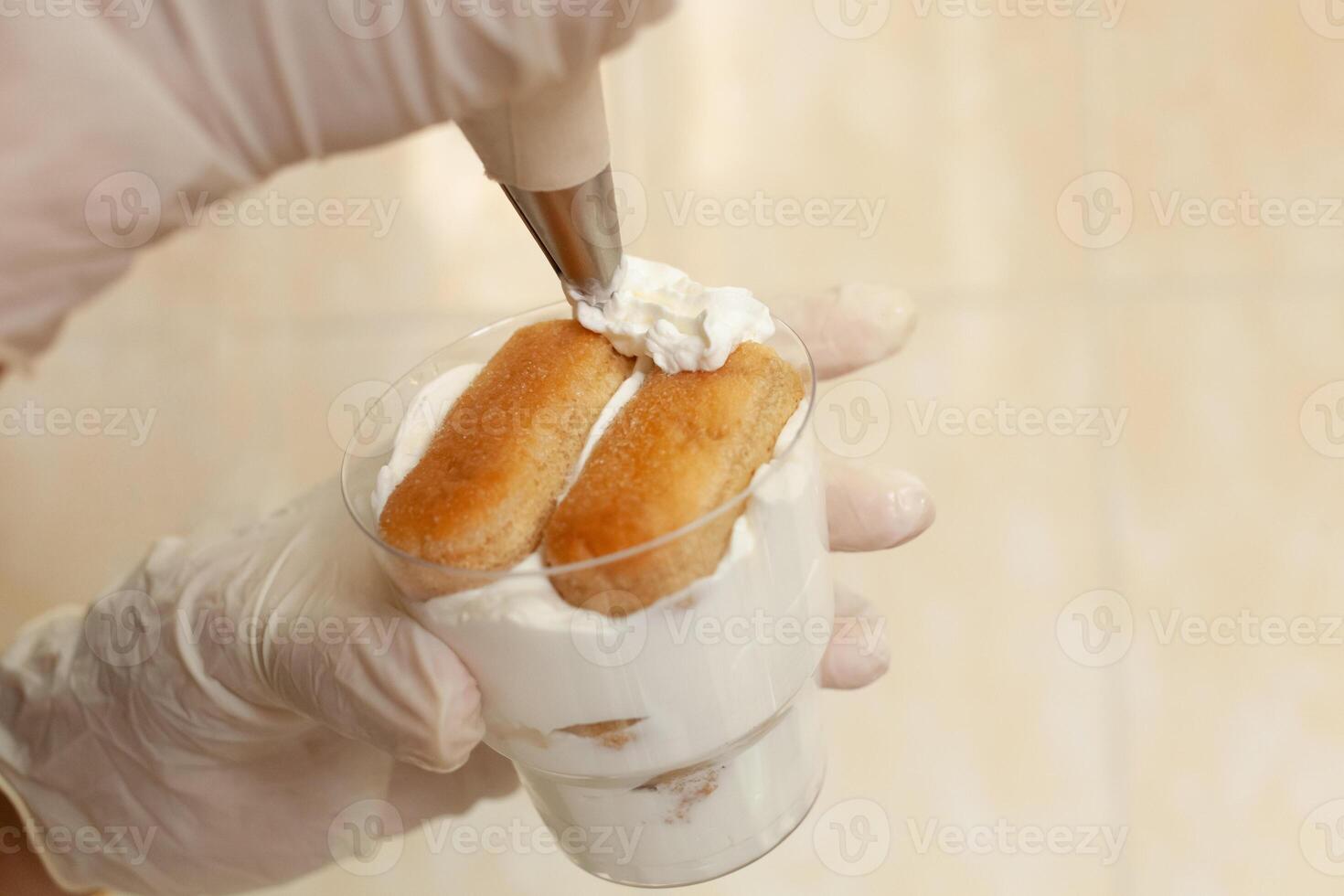 de gebakje chef siert de tiramisu in een glas met geslagen room. foto