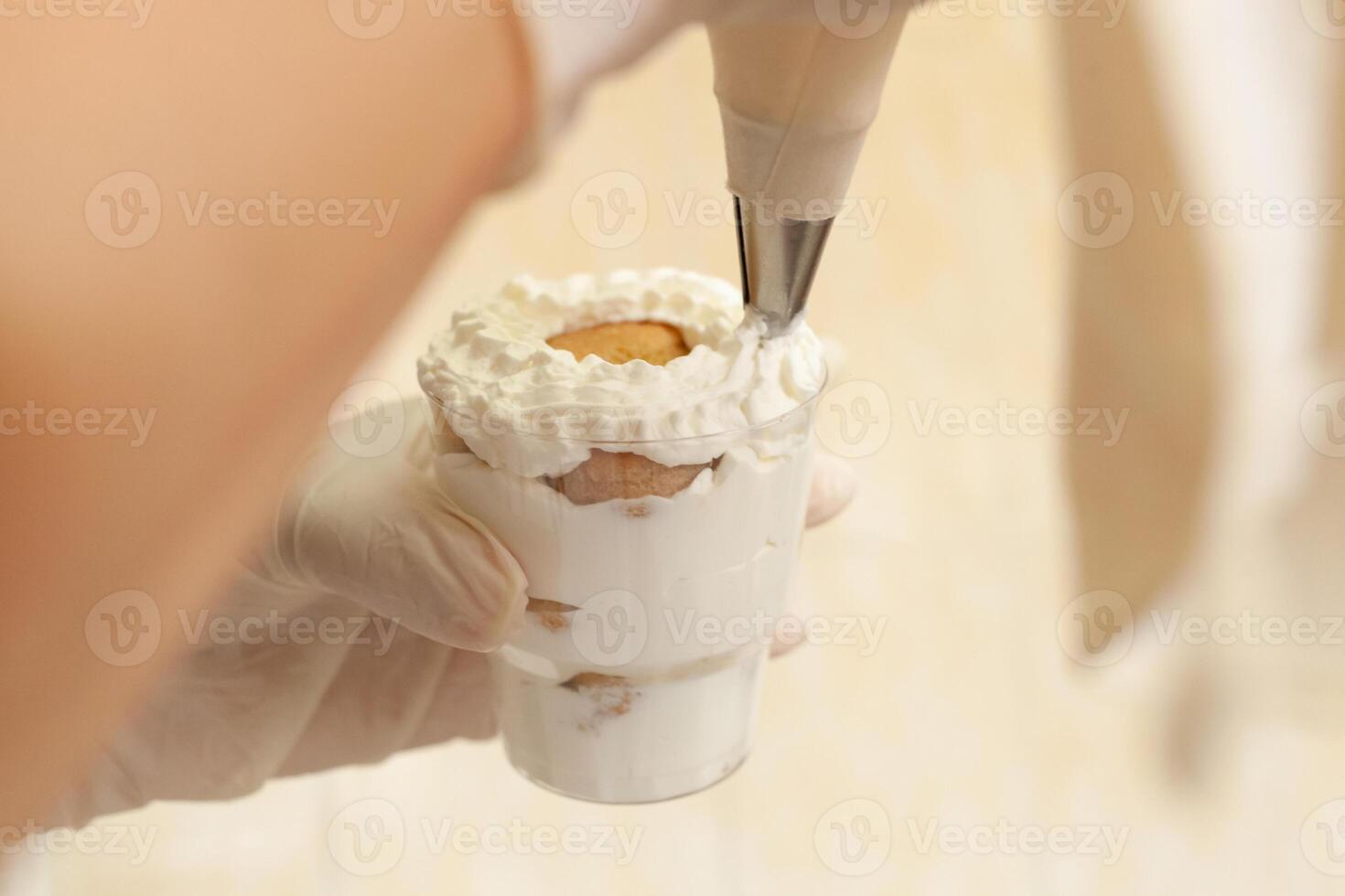 de gebakje chef siert de tiramisu in een glas met geslagen room. foto