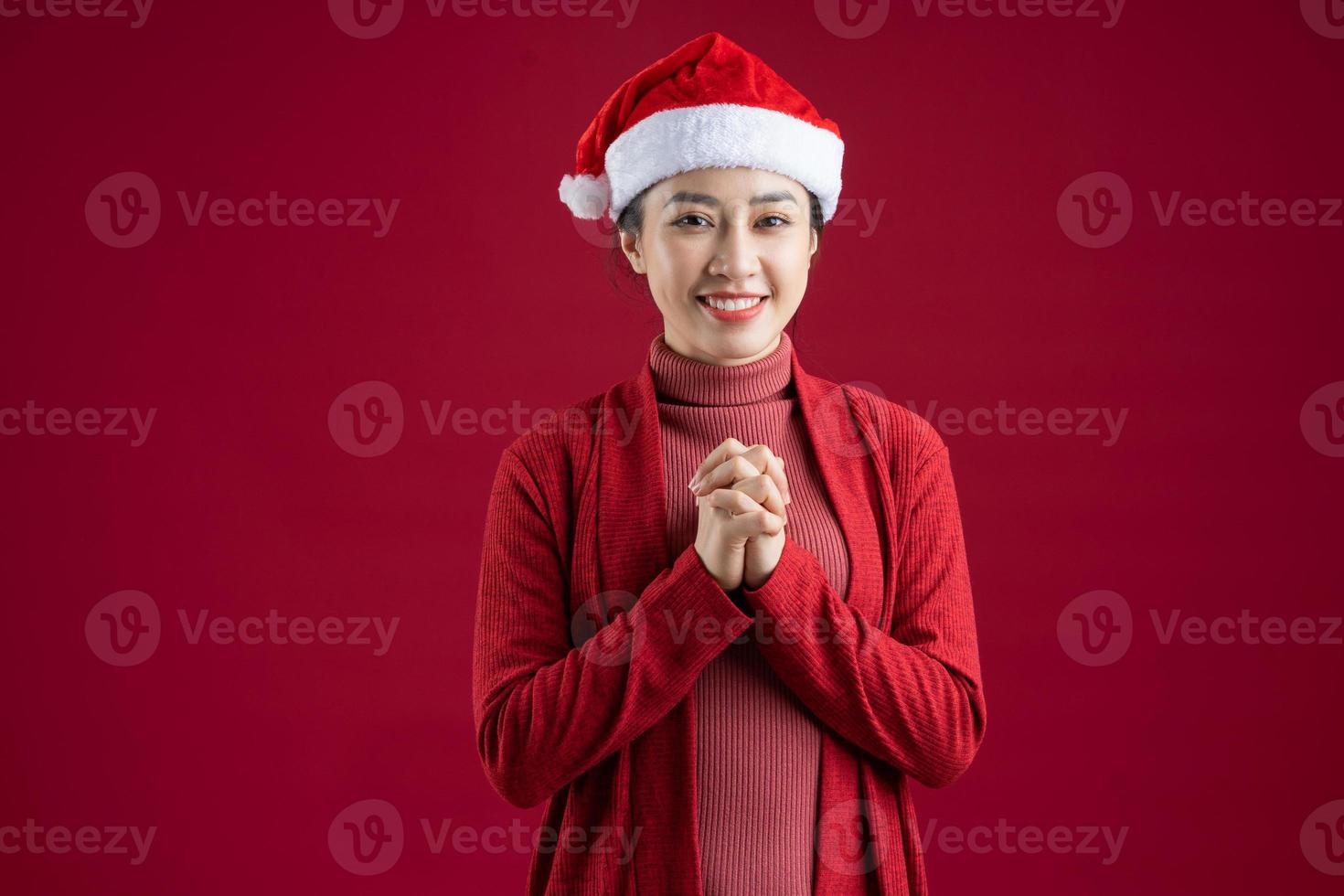 jonge aziatische vrouw die kerstmuts op rode achtergrond draagt foto